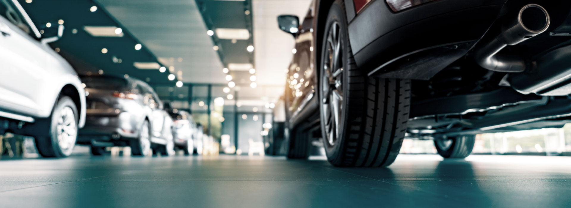 Siisti autoliikkeen showroom lattiatason kuvakulmasta henkilöautojen renkaiden ja kiiltävän lattiapinnan kanssa