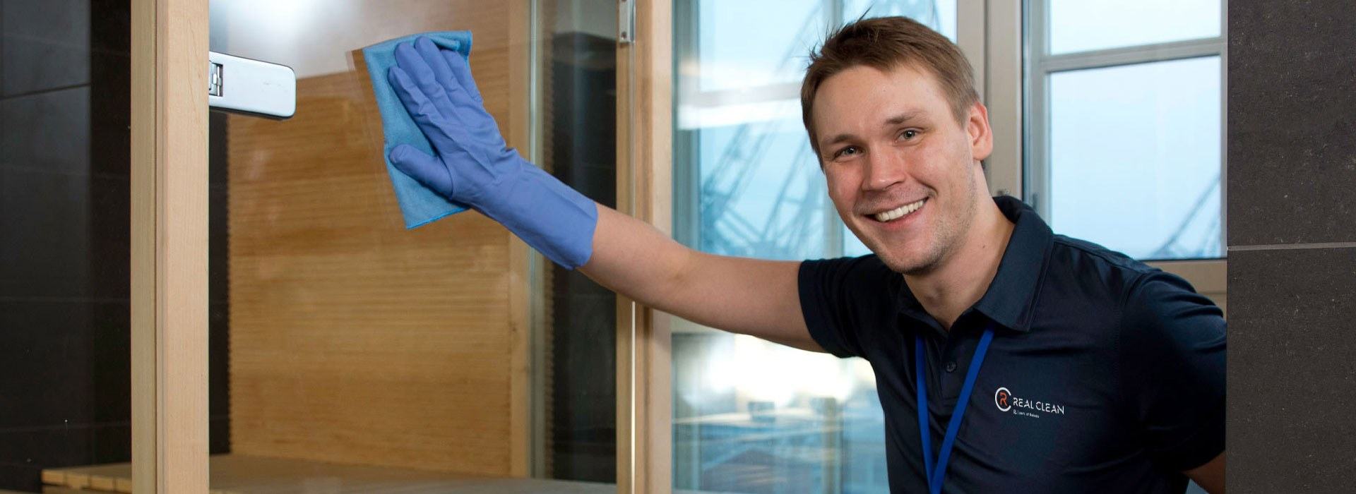 Hymyilevä Real Clean -siivooja puhdistaa lasiovea mikrokuituliinalla